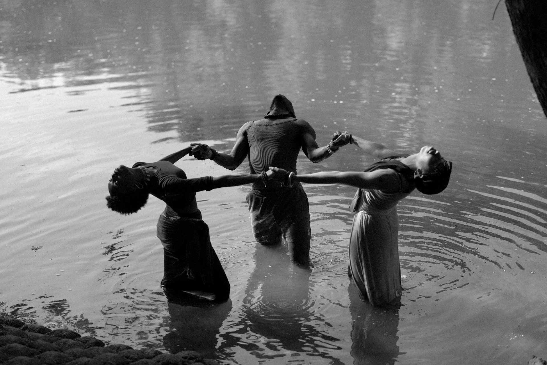 Three figures joined by hands in a river